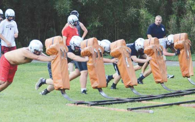 Coach David Mauldwin (right) pushes Black Knights linemen through the sleds during the first official day of practice on August 1.