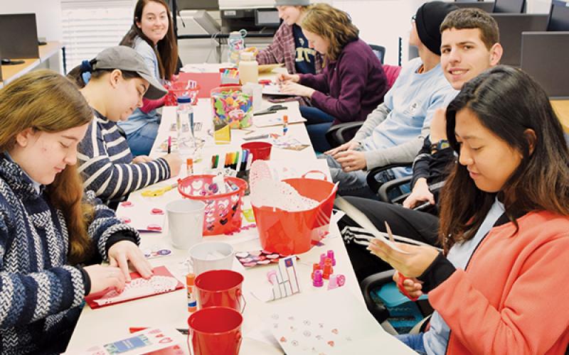 Madison Coffey, Isabelle Handy, Daniella Giese, Ashley Ruston, Catherine Cloutier, Matthew Griffin, Craig Bucci and Slesha Tuladhar (clockwise from bottom left) work on Valentine’s Day cards for troops stationed overseas Friday at the Snowbird  Community Library. Photo by Art Miller/amiller@grahamstar.com