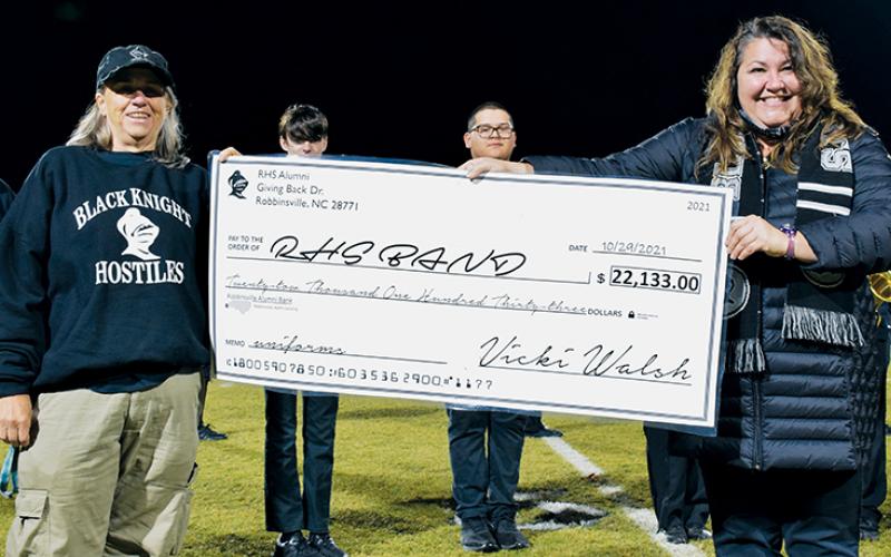 Vicki Walsh (left) presents a check to Robbinsville High School Band before Oct. 29’s home football game against Amber Watkins. At the time, the community-wide effort to raise money for new band uniforms had netted $22,133 – but now, the total has eclipsed $23,000. Photo by Art Miller/amiller@grahamstar.com