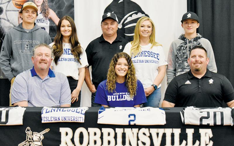 Lady Knights senior Yeika Jimenez (seated, center) signed to play college basketball at Tennessee Wesleyan on May 5. Sitting with Jimenez is Tennessee Wesleyan Lady Bulldogs head coach Jeff Rice (left) and Robbinsville Lady Knights head coach Lucas Ford. Standing in back (from left) are brother Carson Lovin, sister Cambrie Lovin, legal guardians Brandon and Haley Lovin, and brother Luke Lovin.