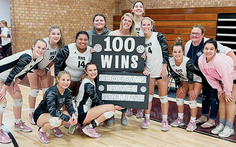 The Robbinsville Lady Knights surround head coach Kadey Phillips on Tuesday, moments after a 4-set victory at Swain County gave Phillips’ her 100th career win. All names are listed from left. Kneeling in front: Suri Watty and Delaney Brooms. Second row: Claire Barlow, Liz Carpenter, Tai Owle, manager Eden Orr, Kadey Phillips, Kensley Phillips, Desta Trammell, assistant coach Dede Brooms and Fala Welch. Standing in back is Aubrie Wachacha. Photos by Kevin Hensley/sports@grahamstar.com