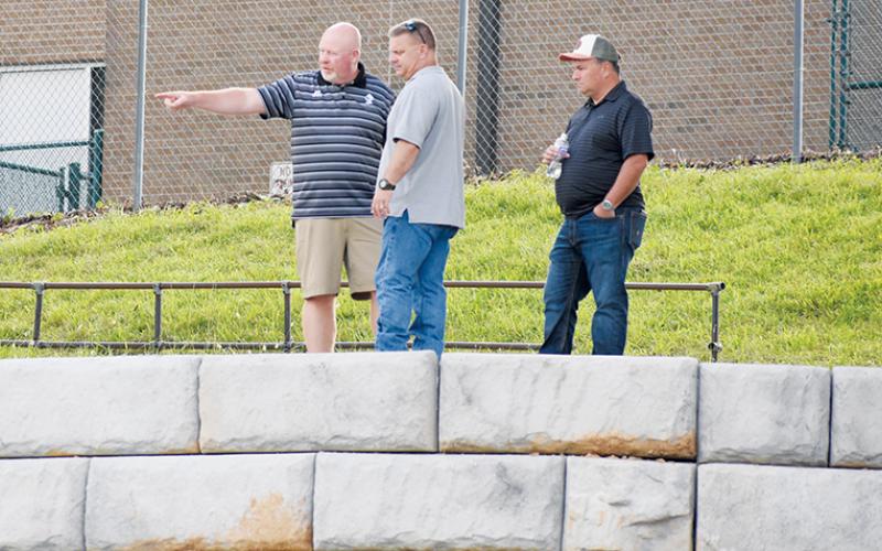 Robbinsville High School Principal David Matheson, Graham County Project Manager Jason Marino and Brandon Lovin of Lovin Contracting (from left) discuss fencing options while standing above a newly-placed retaining wall at Modeal Walsh Memorial (Big Oaks) Stadium on Monday. Photo by Kevin Hensley/sports@grahamstar.com