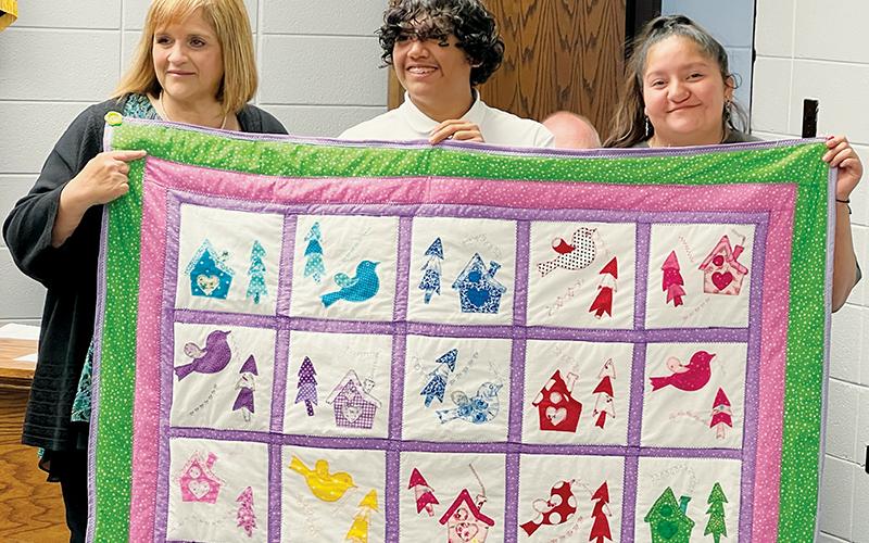 Graham County Schools Superintendent Angie Knight was brought to tears early at Tuesday’s board of education meeting, as she was presented with a quilt made by students at the county’s educational academy. Giving Knight the gift is Emmanuel Conde (center) and Cecelia Maney. Photo by Kevin Hensley/editor@grahamstar.com