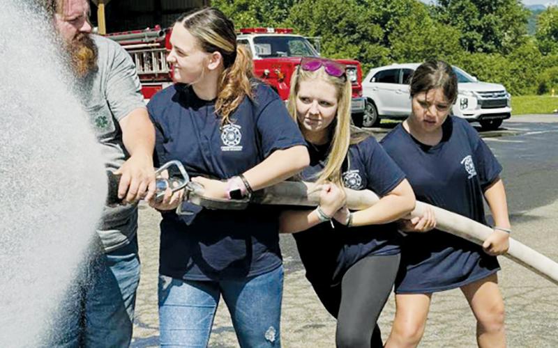 Justin Waldroup assists Kensie Belk, Bella Eddings and Ella Dockery (from left) with a fire hose demonstration during last week's youth fire and rescue academy. Photo courtesy of Graham County Fire and Rescue