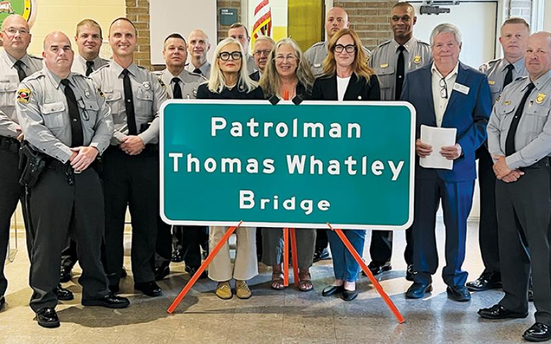 With members of both the North Carolina State Highway Patrol and Department of Transportation in attendance, the nieces of Thomas B. Whatley – Gwen Kinard, Terry Peacock and Pamela Puglisi (center, from left) stand proudly behind a sign dedicating the bridge over the Cheoah River on Old U.S. 129 in Robbinsville in the fallen patrolman's memory. Photos by Kevin Hensley/editor@grahamstar.com