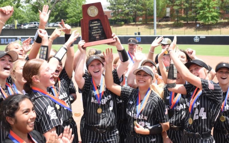 The Robbinsville Lady Knights gather around Daphne Barlow (center), as the sophomore hoists the 1A championship plaque at the conclusion of Saturday's 8-3 victory over Bear Grass Charter.