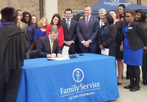 Gov. Roy Cooper signs a package of reforms to North Carolina sexual assault laws Thursday afternoon, during a visit to a domestic violence shelter in Greensboro, as supporters of the legislation look on. Photo by Kate Martin/Carolina Public Press