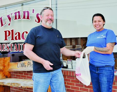 Due to state mandates, dining establishments have been forced to provide  customers with take-out orders only. Mitch Ford (left) is shown picking up a meal from Lynn’s Place employee Haylee Garland on Friday, March 27. Photo by Art Miller/amiller@grahamstar.com