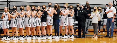 Lady Knights’ basketball players Desta Trammell, Gabby Hooper, Lina Pagan, Kensley Phillips, Halee Anderson, Dallas Garrett, Zoie Shuler, Aubrie Wachacha, Linsey Orr, Karcee Dooley and Yeika Jimenez – as well as head coach Lucas Ford and assistant coaches Kadey Phillips and Eddie Howell (from left) – line up for the playing of the national anthem before the Jan. 5 season opener against Rosman. Photo by Kevin Hensley/editor@grahamstar.com