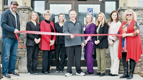Dr. David Booth (center) officially cuts the ribbon outside the re-opened urgent-care facility in Robbinsville on Feb. 16. With Booth are (from left) Graham County Board of Commissioners Chairman Jacob Nelms, nurse Dedie Barker, commissioner Connie Orr, receptionist Brianna Elkins, interim county health director and nurse practitioner Meggan Smith, urgent-care advocate Juanita Colvard, commissioner Natasha Williams and interim county manager Kim Crisp. Photo by Kevin Hensley/editor@grahamstar.com