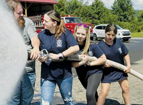 Justin Waldroup assists Kensie Belk, Bella Eddings and Ella Dockery (from left) with a fire hose demonstration during last week's youth fire and rescue academy. Photo courtesy of Graham County Fire and Rescue