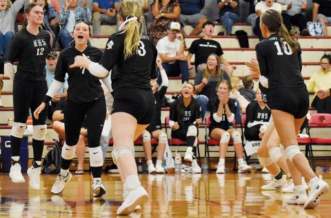 Members of the Robbinsville Lady Knights volleyball team and fanbase erupt in celebration after a big point was scored during Aug. 28's five-set victory at Andrews. Players visibly celebrating on the floor are Chloe Adams (10), Ella McGuire (7), Daphne Barlow (3) and Izabel Haney (10). Photo by Bella Eddings/The Graham Star