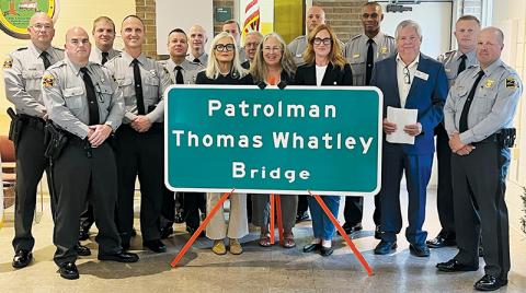 With members of both the North Carolina State Highway Patrol and Department of Transportation in attendance, the nieces of Thomas B. Whatley – Gwen Kinard, Terry Peacock and Pamela Puglisi (center, from left) stand proudly behind a sign dedicating the bridge over the Cheoah River on Old U.S. 129 in Robbinsville in the fallen patrolman's memory. Photos by Kevin Hensley/editor@grahamstar.com