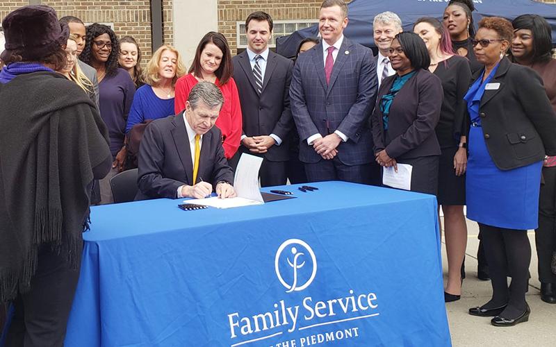 Gov. Roy Cooper signs a package of reforms to North Carolina sexual assault laws Thursday afternoon, during a visit to a domestic violence shelter in Greensboro, as supporters of the legislation look on. Photo by Kate Martin/Carolina Public Press