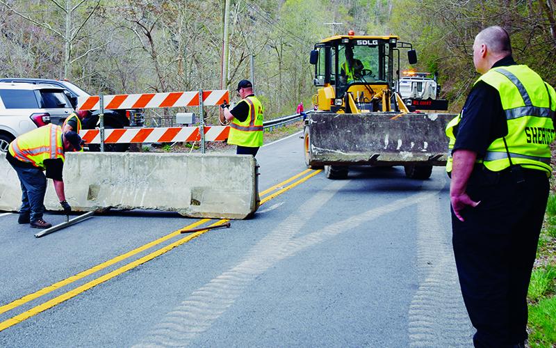 Under the watchful eye of Graham County Deputy Dennis Crisp (right), a pair of Graham County Land Employees install a concrete barrier on U.S. 129 – near Cheoah Dam – on Friday. The barricade – along with another on the Cherohala Skyway – were removed Sunday and replaced with manned checkpoints.