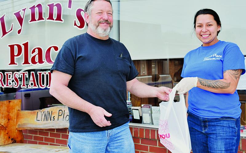 Due to state mandates, dining establishments have been forced to provide  customers with take-out orders only. Mitch Ford (left) is shown picking up a meal from Lynn’s Place employee Haylee Garland on Friday, March 27. Photo by Art Miller/amiller@grahamstar.com