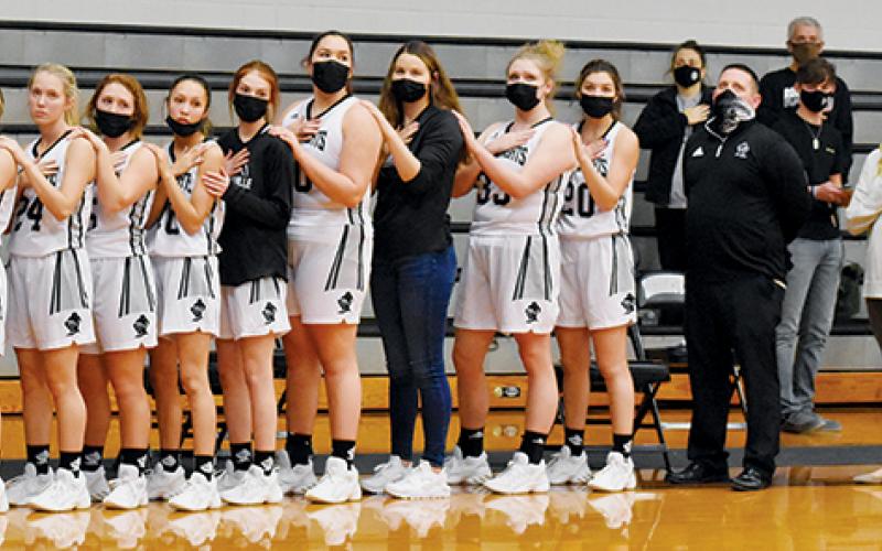 Lady Knights’ basketball players Desta Trammell, Gabby Hooper, Lina Pagan, Kensley Phillips, Halee Anderson, Dallas Garrett, Zoie Shuler, Aubrie Wachacha, Linsey Orr, Karcee Dooley and Yeika Jimenez – as well as head coach Lucas Ford and assistant coaches Kadey Phillips and Eddie Howell (from left) – line up for the playing of the national anthem before the Jan. 5 season opener against Rosman. Photo by Kevin Hensley/editor@grahamstar.com