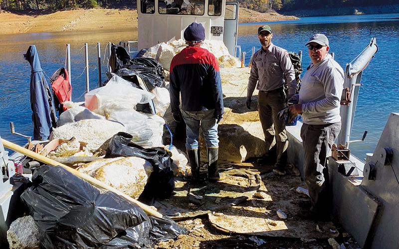 Three volunteers in the annual Fontana Lakeshore Cleanup haul garbage aboard their vessel. The event was held from Friday-Sunday and removed more than 170,000 pounds of trash from the lake.