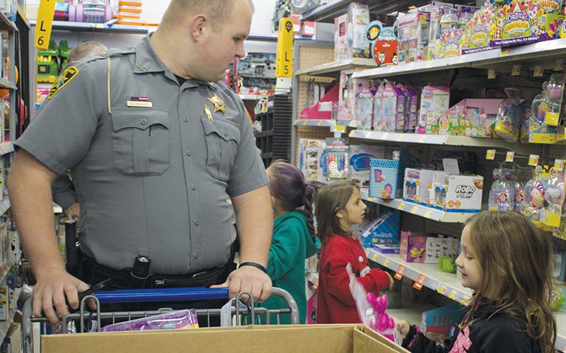 Graham County Sheriff’s Office transport officer Chase Hughes looks on as one of the Shop with a Cop participants gleefully examines a potential gift. Photo by Charlie Benton/news@grahamstar.com