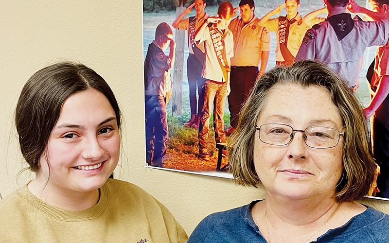 Willow (left) and Lisa Trantham pose beside a news photo displayed at The Graham Star. The photo includes Gentry Trantham, left in the photo, saluting during a Boy Scouts flag-burning ceremony. Photo by Randy Foster/news@grahamstar.com