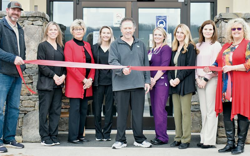 Dr. David Booth (center) officially cuts the ribbon outside the re-opened urgent-care facility in Robbinsville on Feb. 16. With Booth are (from left) Graham County Board of Commissioners Chairman Jacob Nelms, nurse Dedie Barker, commissioner Connie Orr, receptionist Brianna Elkins, interim county health director and nurse practitioner Meggan Smith, urgent-care advocate Juanita Colvard, commissioner Natasha Williams and interim county manager Kim Crisp. Photo by Kevin Hensley/editor@grahamstar.com