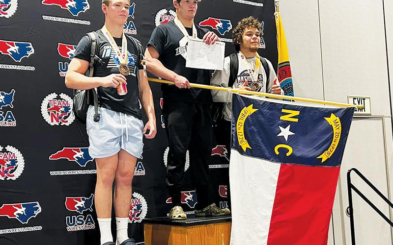 Rising Black Knights senior Kage Williams proudly displays the North Carolina state flag while standing atop the podium at the USA Wrestling Southeast Regionals in Cherokee on May 28. Williams went 5-0 in his 195-pound bracket to win Robbinsville’s inaugural Southeastern title. Photo courtesy of Peak Wrestling