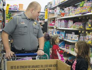 Graham County Sheriff’s Office transport officer Chase Hughes looks on as one of the Shop with a Cop participants gleefully examines a potential gift. Photo by Charlie Benton/news@grahamstar.com
