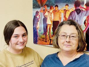 Willow (left) and Lisa Trantham pose beside a news photo displayed at The Graham Star. The photo includes Gentry Trantham, left in the photo, saluting during a Boy Scouts flag-burning ceremony. Photo by Randy Foster/news@grahamstar.com
