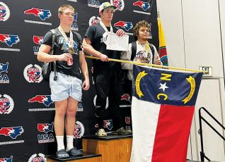 Rising Black Knights senior Kage Williams proudly displays the North Carolina state flag while standing atop the podium at the USA Wrestling Southeast Regionals in Cherokee on May 28. Williams went 5-0 in his 195-pound bracket to win Robbinsville’s inaugural Southeastern title. Photo courtesy of Peak Wrestling