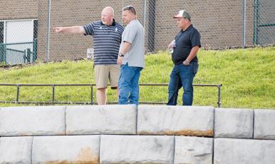 Robbinsville High School Principal David Matheson, Graham County Project Manager Jason Marino and Brandon Lovin of Lovin Contracting (from left) discuss fencing options while standing above a newly-placed retaining wall at Modeal Walsh Memorial (Big Oaks) Stadium on Monday. Photo by Kevin Hensley/sports@grahamstar.com
